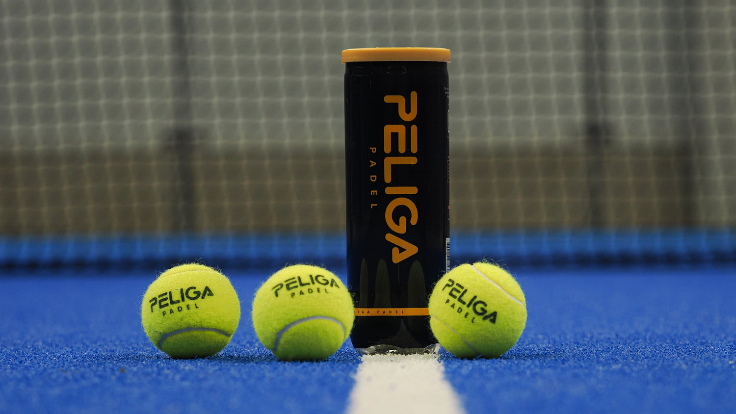 Three Peliga tennis balls and a canister on a blue court with a net in the background.
